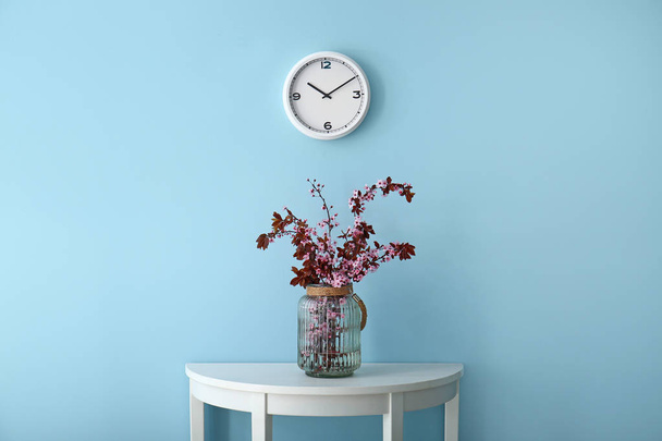 Ваза з красивими квітучими гілками на столі біля кольорової стіни
 - Фото, зображення