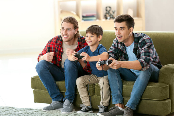 Couple gay avec enfant adopté jouant à un jeu vidéo à la maison
 - Photo, image