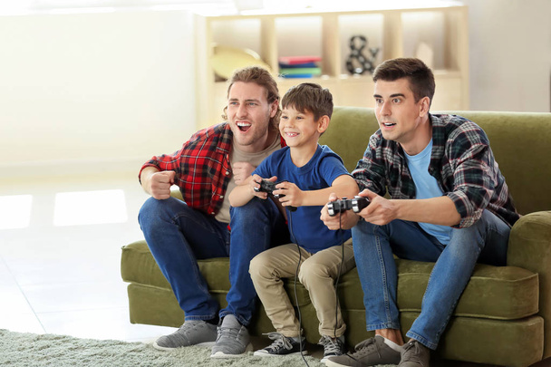 Голубая пара с усыновленным ребенком, играющая в видеоигры дома
 - Фото, изображение