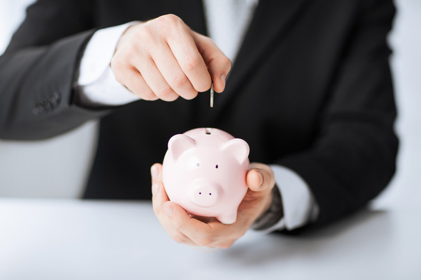Man putting coin into small piggy bank - Photo, image