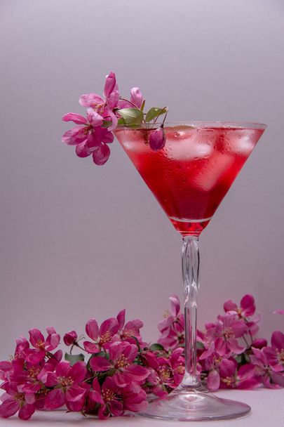 Le verre de martini est rempli d'une boisson alcoolisée rouge avec de la glace et décoré avec des branches de fleurs roses de printemps
. - Photo, image
