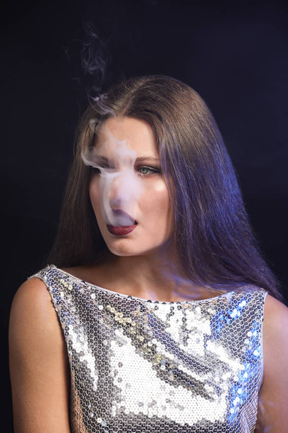 Esmer arka planda sigara içen genç bir kadın - Fotoğraf, Görsel