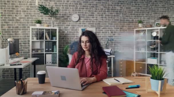 Time-lapse of girl working with laptop in creative office while coworkers moving - Filmagem, Vídeo