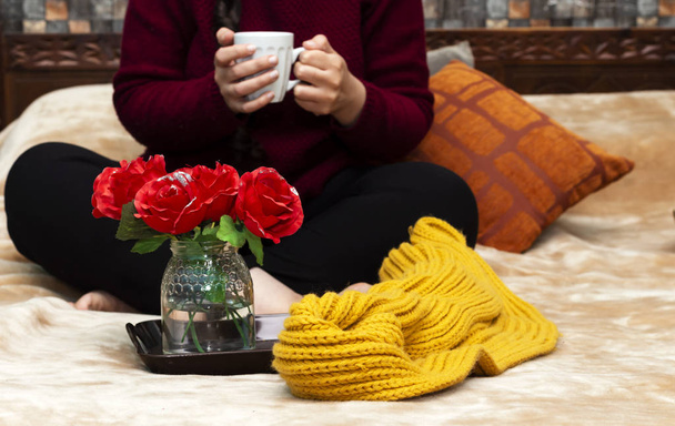 vrouw die op het bed zit, koffie drinkt, rozen vaas in dienblad tijdens de ochtend - Foto, afbeelding
