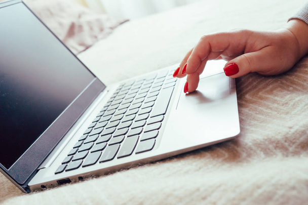 Femme main avec des ongles rouges sur le clavier de l'ordinateur portable, dame en utilisant un ordinateur portable sur la couverture de lit
 - Photo, image
