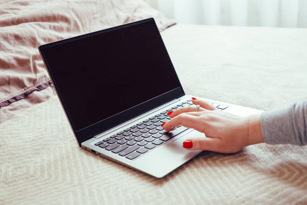 Mano de las mujeres con clavos rojos en el teclado del ordenador portátil, señora usando el ordenador portátil en la cama manta
 - Foto, imagen