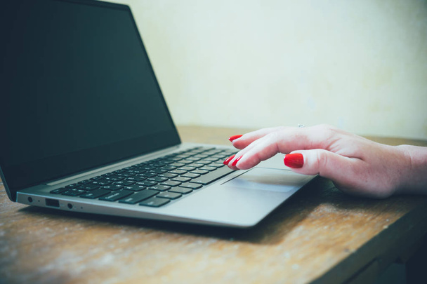 Laptop klavyesinde kırmızı tırnaklı kadın eli, eski tip masada dizüstü bilgisayar kullanan kadın. - Fotoğraf, Görsel