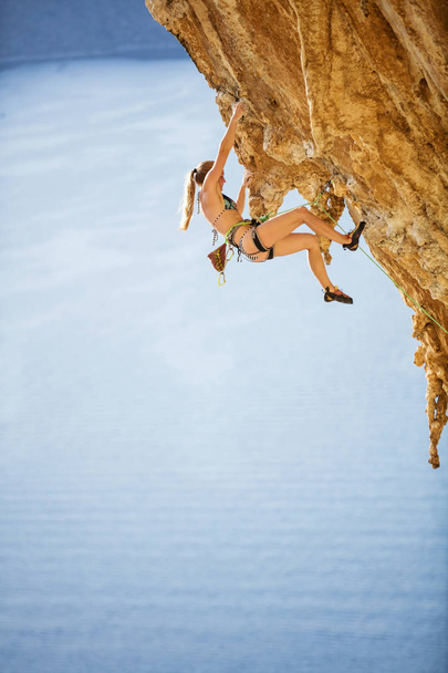 張り出した崖の上に挑戦的なルートを登るビキニの若い女性 - 写真・画像