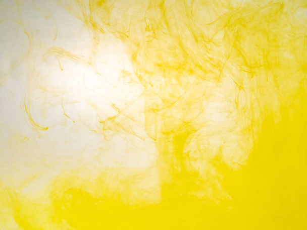 Clouds of acrilic paint swirling in water, close up view. Blurred background. Drop of yellow ink dissolving into water, abstract pattern. Transformation of ink droplet in liquid, abstract background. - Fotografie, Obrázek