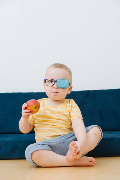 Little toddler boy in lazy eye patch with an apple in hand - Foto, Bild