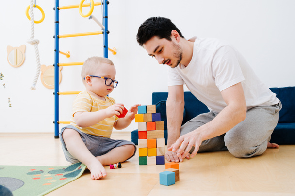 Father with a small toddler son are building tower from toy cubes - Foto, afbeelding