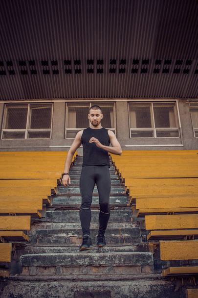 Caucasian man trains in running on the stairs. Track and field runner in sport uniform training outdoor. athlete, top view. step exercise. steps down. vertical - Foto, Imagen