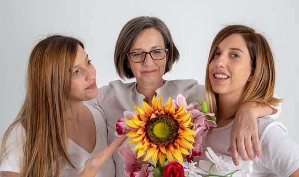 mother and two twin sisters enjoy in very funny attitude with a big sunflower in their hands - Photo, Image
