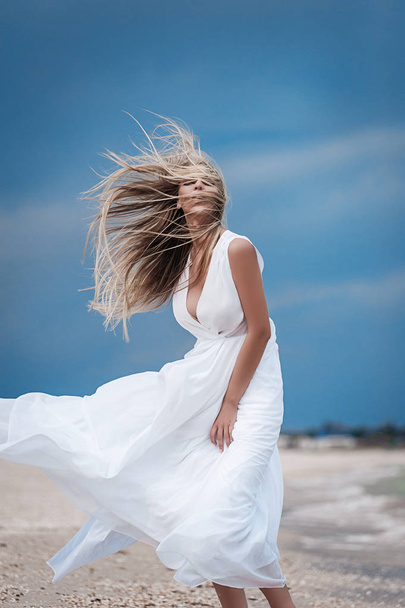 Blonde in a white dress on the beach - Фото, изображение