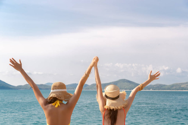Beautiful young women holding hands, raise up hands together. They are friend and always love traveling together when they get holiday or vacation time in summer season. sea sky mountain background - Photo, Image