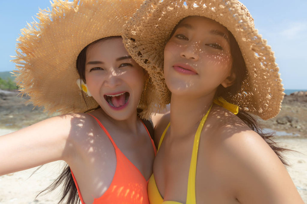 Beautiful young women have summer holiday or vacation time at beautiful beach. Pretty girls get enjoying their summer season life together. Asian women get happiness and fun. They wear bikini, hats. - Photo, Image