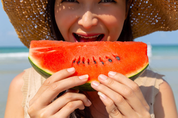 Charmante mooie jonge vrouw die watermeloen eet om af te koelen en haar dorst te lessen in het zomerseizoen op het strand. Het ziet er sappig en zoet uit. Aantrekkelijk mooi Aziatisch meisje krijgt geluk met lachebekje - Foto, afbeelding