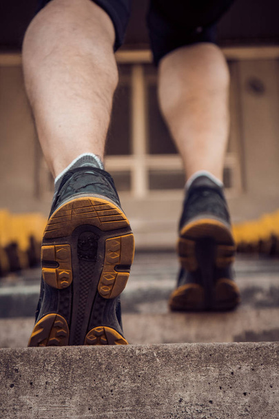 man trains in running on the stairs. Track and field runner in sport uniform training outdoor. athlete, below view. step exercises. vertical. pumped up shanks close up - Fotografie, Obrázek