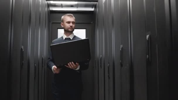 Hombre serio caminando y controlar la línea de servidores que sostiene el ordenador portátil
 - Metraje, vídeo