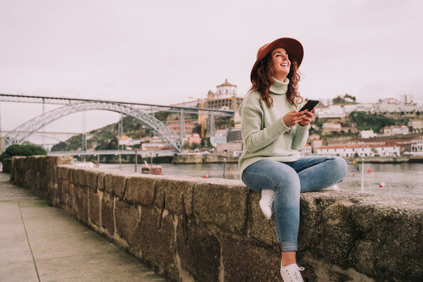 A tourist woman laughing with the phone between her hands next to the bridge of Porto - 写真・画像