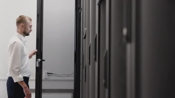 Hombre abierto servidor rack y escribir en el ordenador portátil en la sala de centro de datos
 - Metraje, vídeo