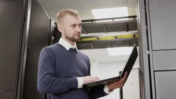 System administrator holding laptop standing before server rack - Footage, Video