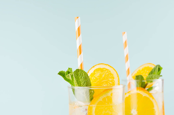 Summer fresh drinks with oranges, ice cubes, green mint and striped straw in wineglass on blue wall, top section, edge. - Photo, image