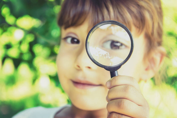 The child is looking in a magnifying glass. Increase. selective focus. - Foto, immagini