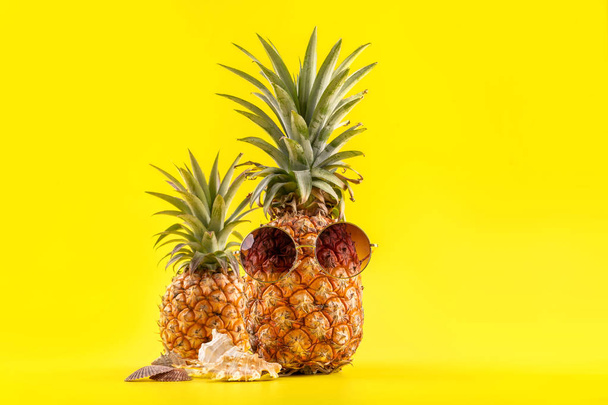Creative pineapple looking up with sunglasses and shell isolated on yellow background, summer vacation beach idea design pattern, copy space close up - Foto, immagini