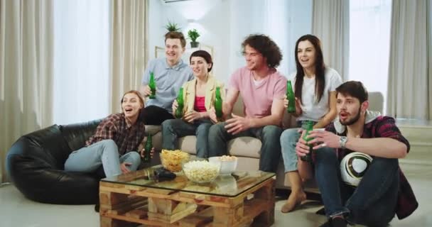 Çok heyecanlı arkadaşlar bir oturma odasının ortasında tv'de bir futbol maçı izlemeye hazırlanıyorlar bira içiyorlar ve birlikte vakit geçiriyorlar. - Video, Çekim