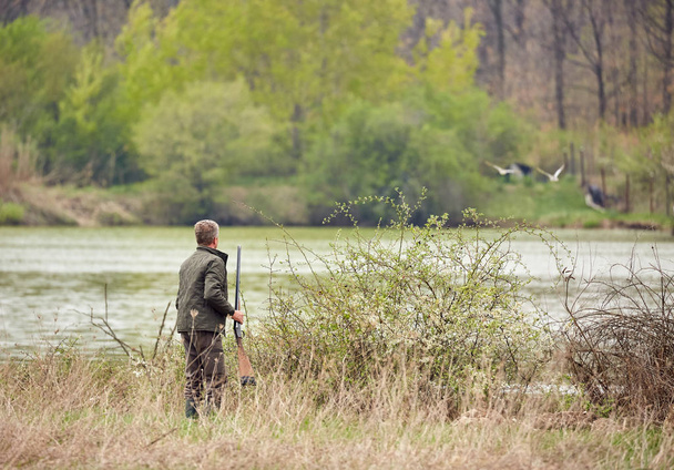 Hunter sneaking on wild ducks on a lake - Фото, изображение