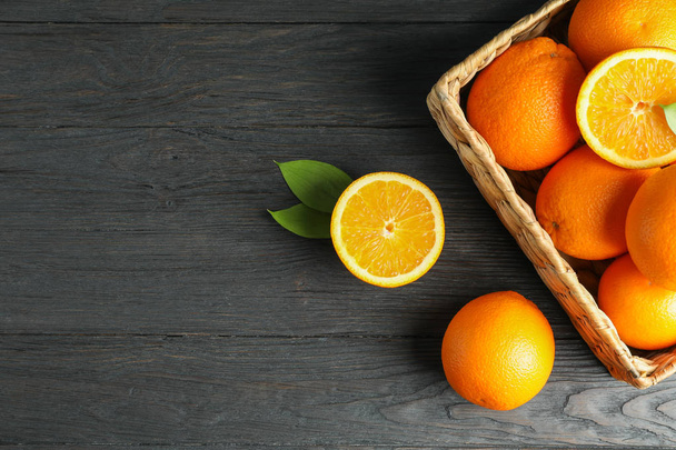 Wicker basket with ripe oranges on wooden table. Top view, space - Фото, изображение