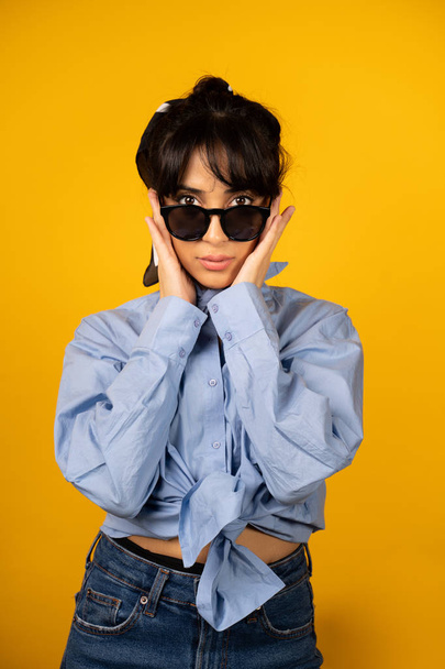 Young girl with in sunglasses posing for a photo on yellow background. - Foto, afbeelding