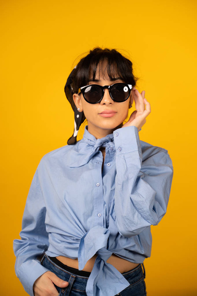 Young girl with in sunglasses posing for a photo on yellow background. - Фото, зображення