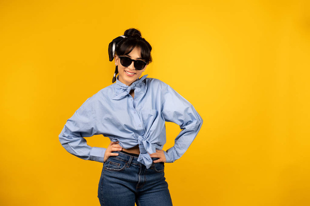 Young girl with in sunglasses posing for a photo on yellow background. - Φωτογραφία, εικόνα