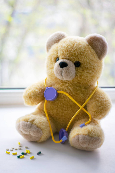 Cute teddy bear with a phonendoscope next to pills in the pediatric healthcare concept - Photo, Image