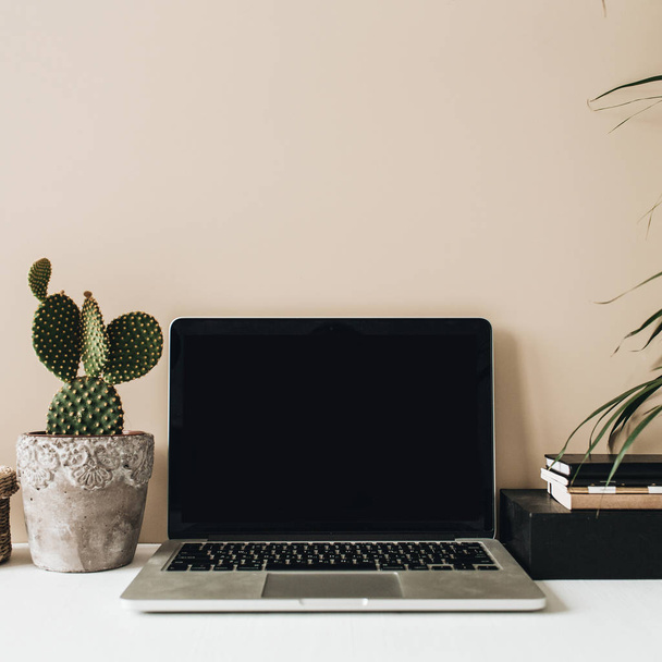 Minimalist home office desk workspace with laptop, cactus and palm on beige background. Front view copy space blank mock up. - Photo, Image