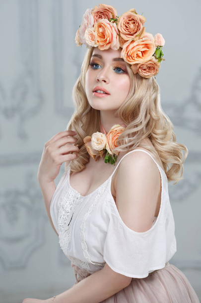 Fashion beauty portrait of a cute smiling blonde girl in a wreath of tea roses. - Φωτογραφία, εικόνα