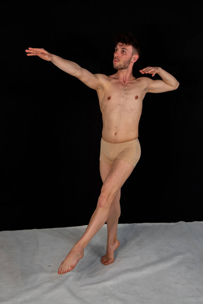 Gimnastyce stanowią kaukaski człowiek tańczy w studiu z tworzywa sztucznego rąk i nóg pozycji. Atrakcyjny młody człowiek pokazuje nowoczesne potańce, na czarnym tle. - Zdjęcie, obraz