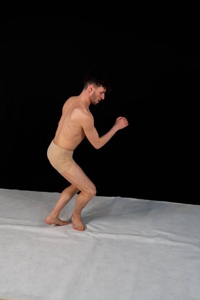 La pose gymnastique de l'homme caucasien danse en studio avec des positions de main et de jambe en plastique. Le jeune homme séduisant montre des poses de danse moderne, sur un fond noir
. - Photo, image