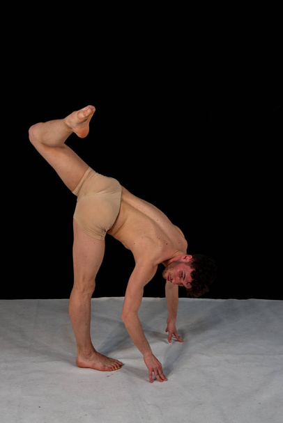 Gymnastická póza kavkazského muže tancuje ve studiu s plastovými polohami rukou a nohou. Atraktivní mladý muž ukazuje moderní taneční pozice na černém pozadí. - Fotografie, Obrázek