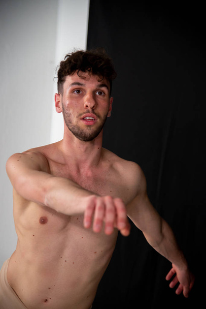 Half-naked portrait of a young male dancer, in movements relating to dancing with his hands. The attractive young man with beard in modern dance demonstrations on a black background. - Photo, Image