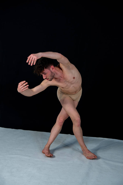 Gimnastyce stanowią kaukaski człowiek tańczy w studiu z tworzywa sztucznego rąk i nóg pozycji. Atrakcyjny młody człowiek pokazuje nowoczesne potańce, na czarnym tle. - Zdjęcie, obraz