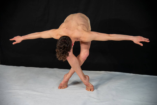 Male dancer bows at the end of the show, practicing in the studio against a black background. The attractive young muscular man has crossed legs and open arms. - Photo, Image
