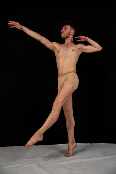 The gymnastic pose of the Caucasian man dances in the studio with plastic hand and leg positions. The attractive young man shows modern dance poses, on a black background. - Fotó, kép