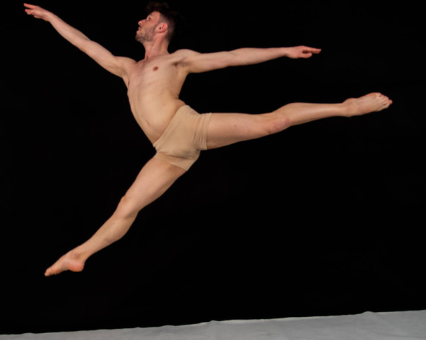 Joven bailarín masculino fotografiado mientras saltaba en la mosca gimnástica. El atractivo joven en las demostraciones de danza moderna, bailando en el estudio sobre un fondo negro
. - Foto, imagen