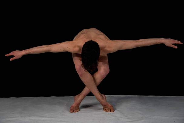 Male dancer bows at the end of the show, practicing in the studio against a black background. The attractive young muscular man has crossed legs and open arms. - Photo, Image