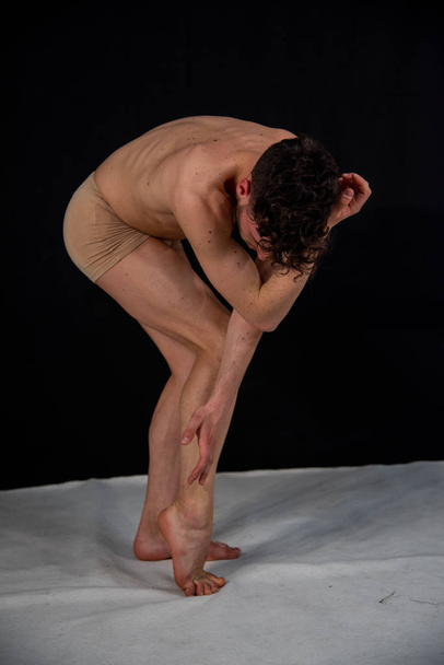 The gymnastic pose of the Caucasian man dances in the studio with plastic hand and leg positions. The attractive young man shows modern dance poses, on a black background. - Photo, Image