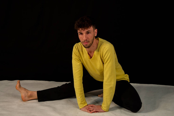 Tänzer mit schwarzer Hose und gelbem Trikot vor schwarzem Hintergrund. der junge attraktive Mann zeigt die Posen im Yoga. - Foto, Bild