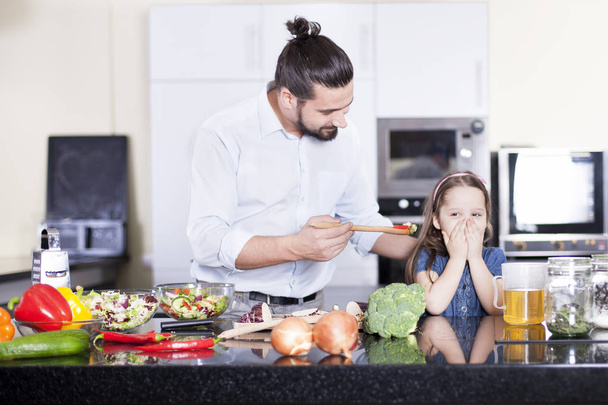 小さな女の子は、料理や台所で一緒に昼食を食べながらサラダを食べることを拒否 - 写真・画像
